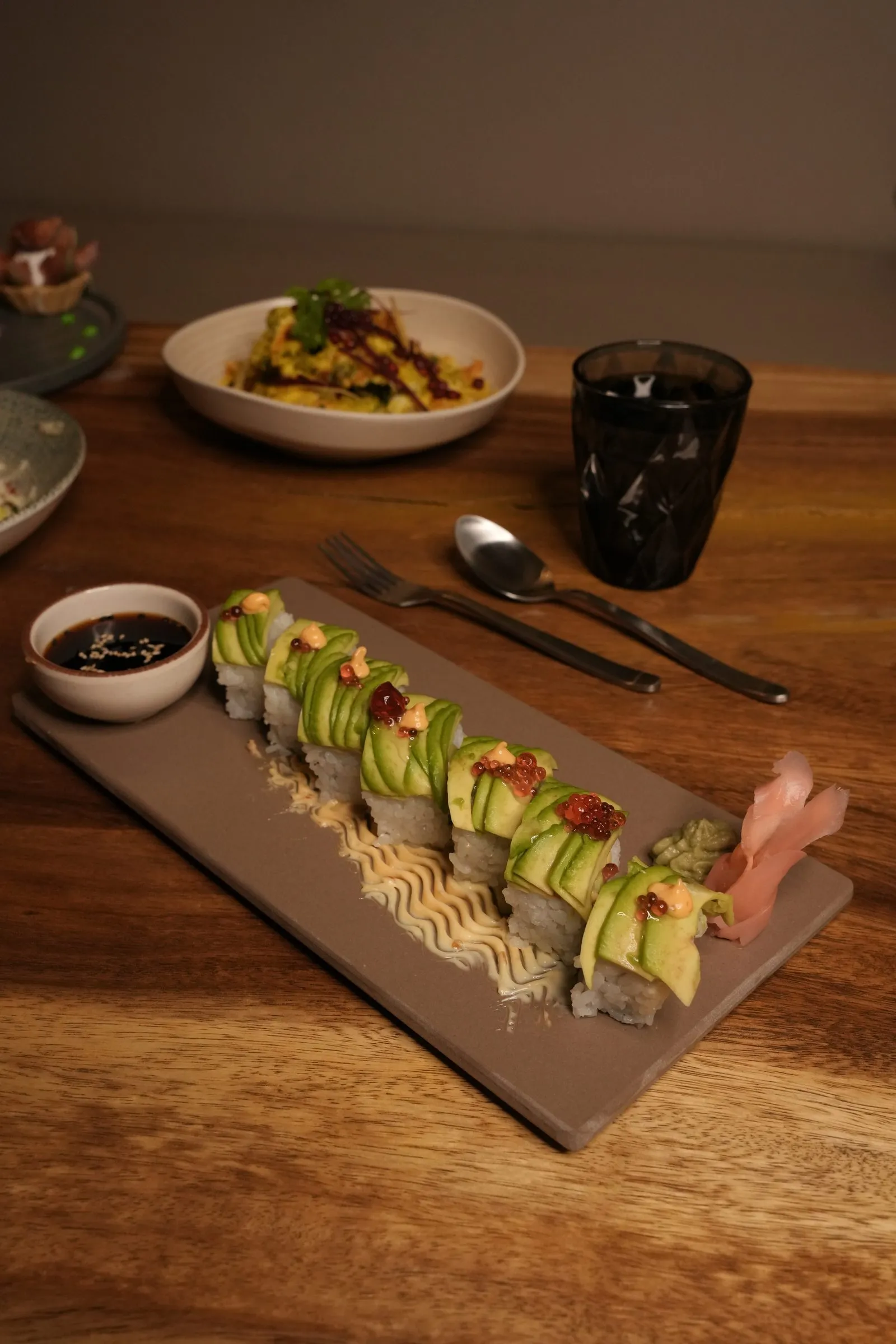 Sushi rolls topped with avocado on a slate board