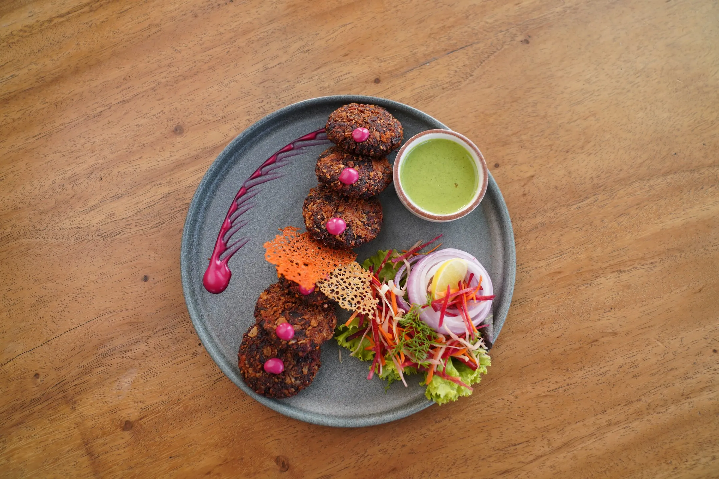 Round kebabs on a slate plate with a beetroot swirl and mint chutney, seen from above