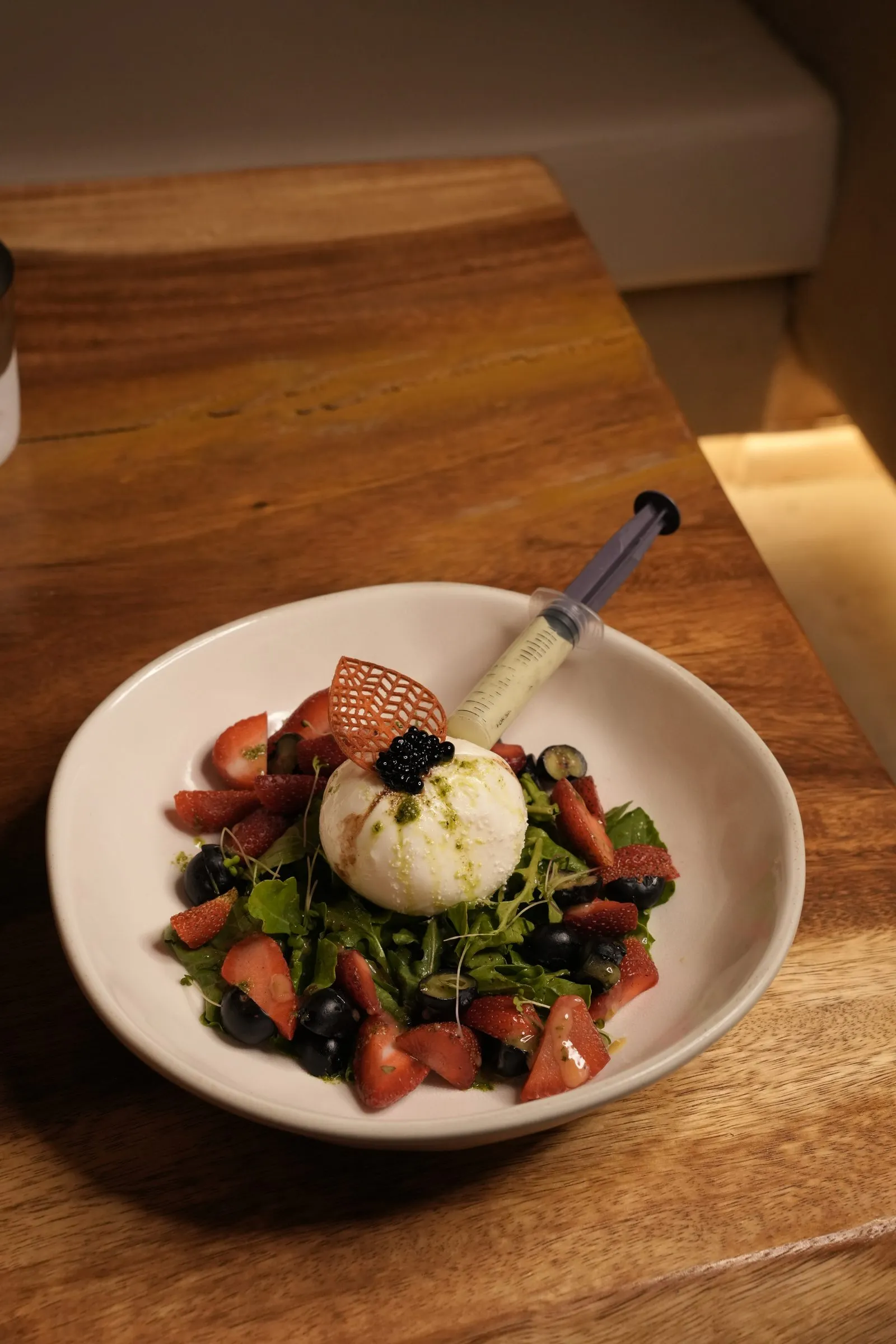 A burrata salad with berries and greens, finished with a dressing-filled syringe