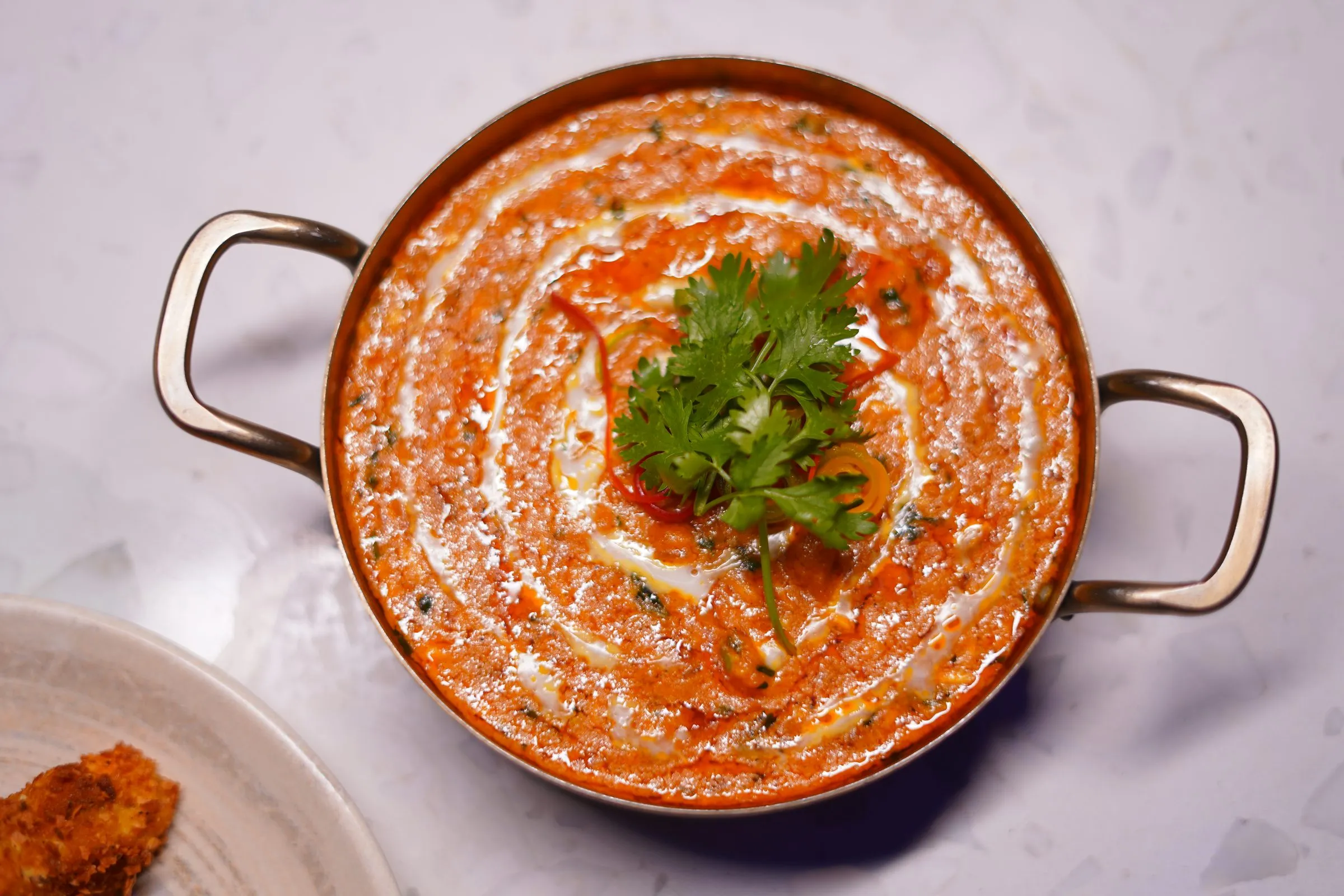 A creamy tomato curry in a copper handi, topped with fresh coriander