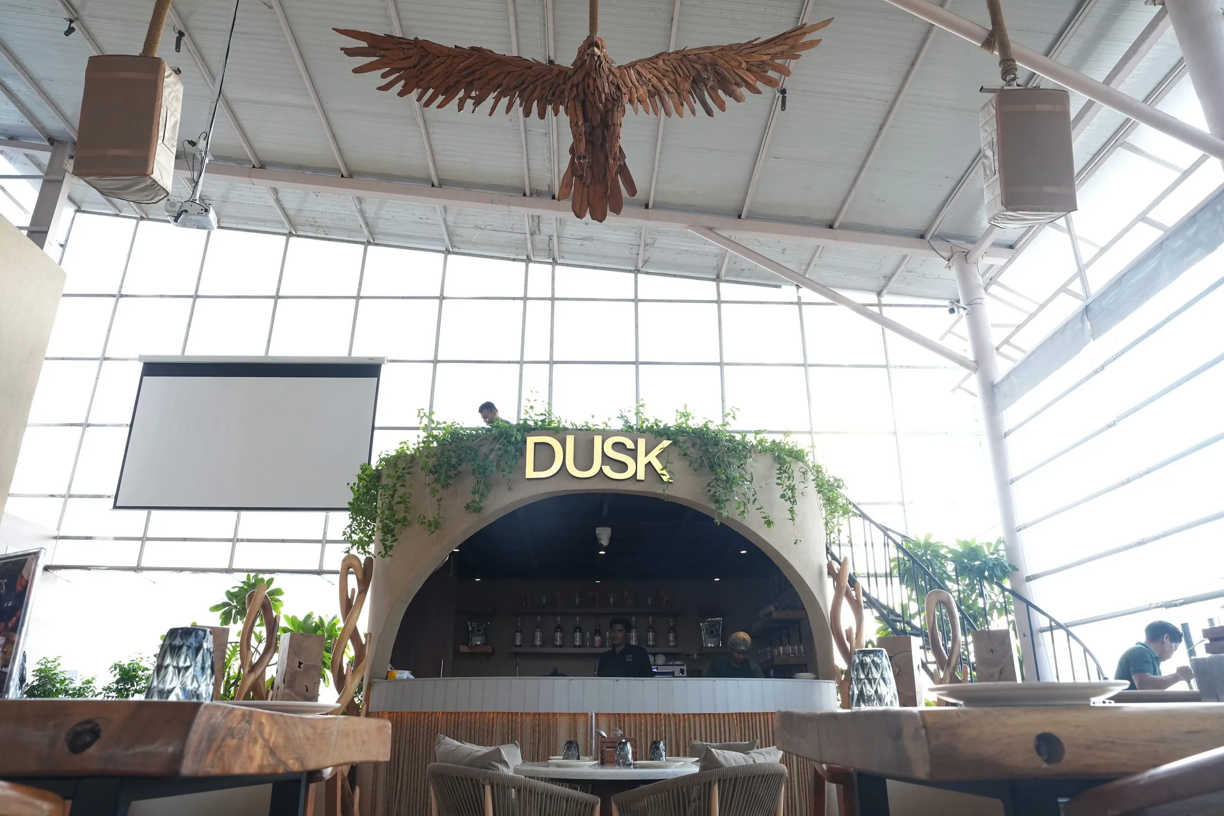 The glowing DUSK sign above the counter, with a driftwood eagle hanging from the glass roof