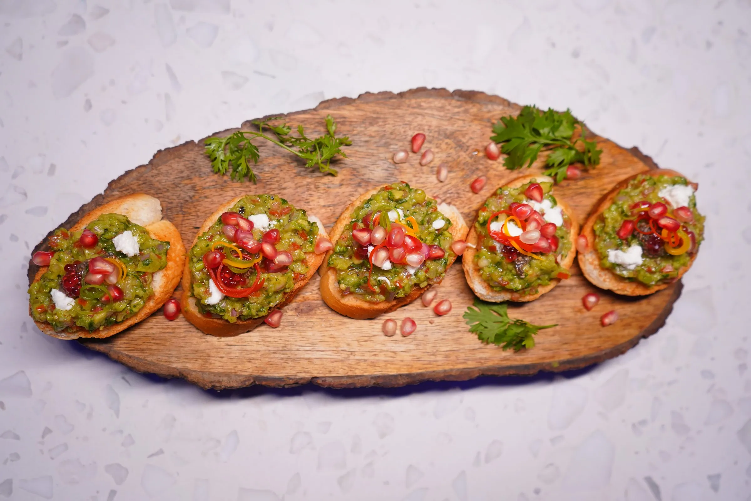 Crostini topped with guacamole and pomegranate on a live-edge board