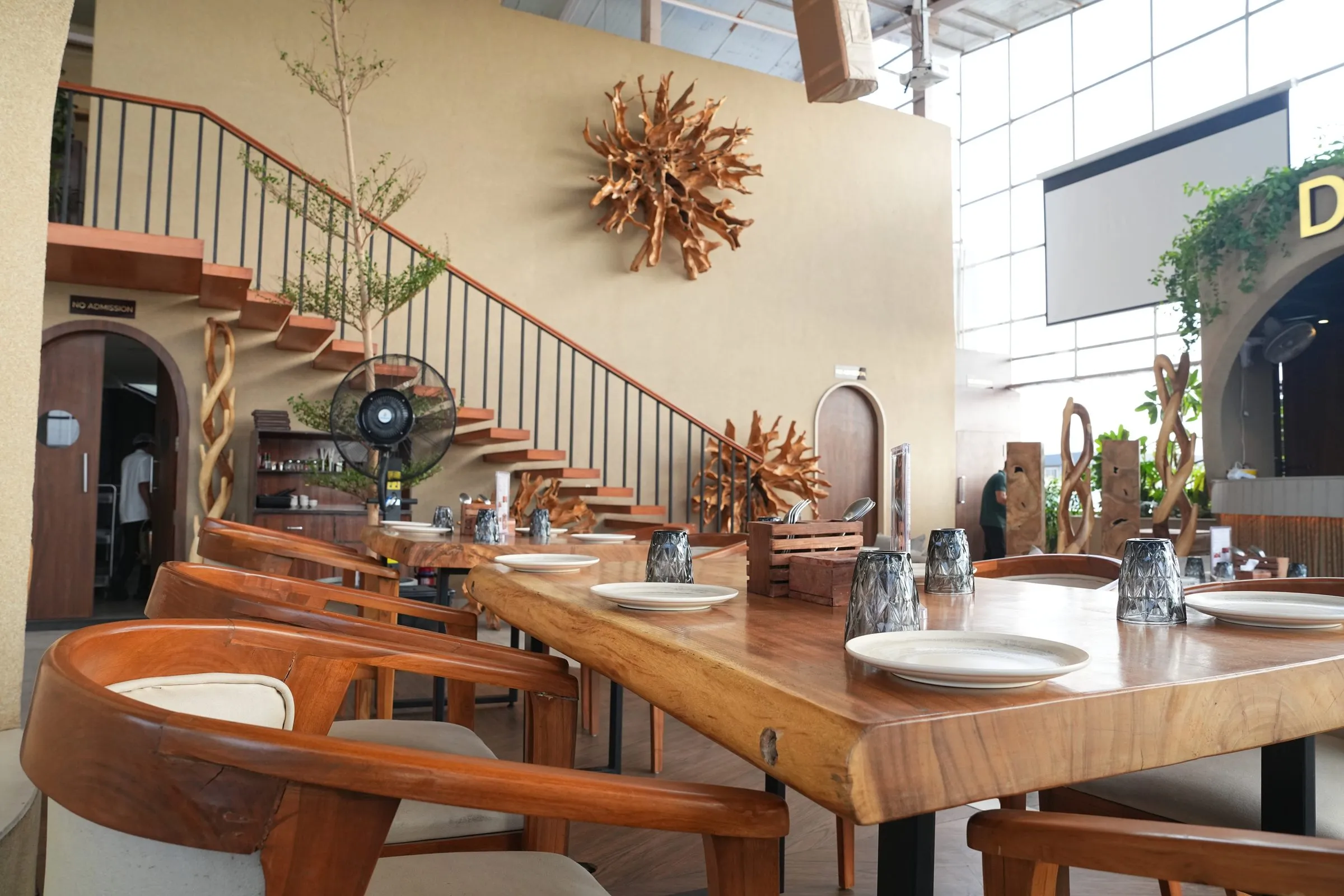 A long live-edge wooden table beside the staircase and root sunburst