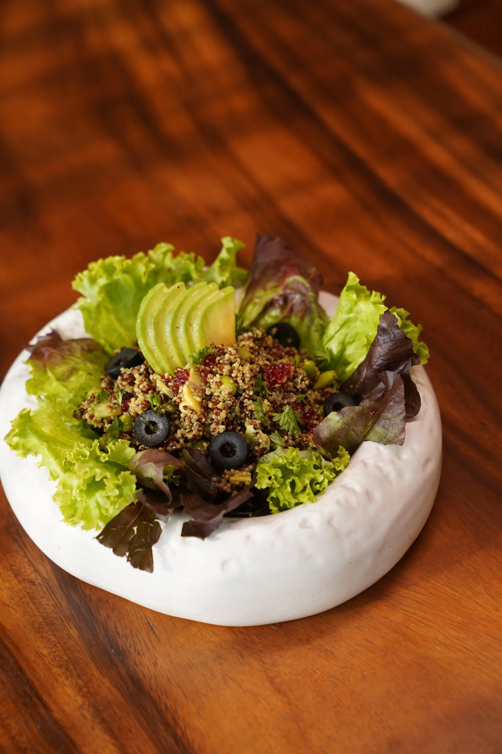 A quinoa bowl with sliced avocado, black olives and crisp lettuce