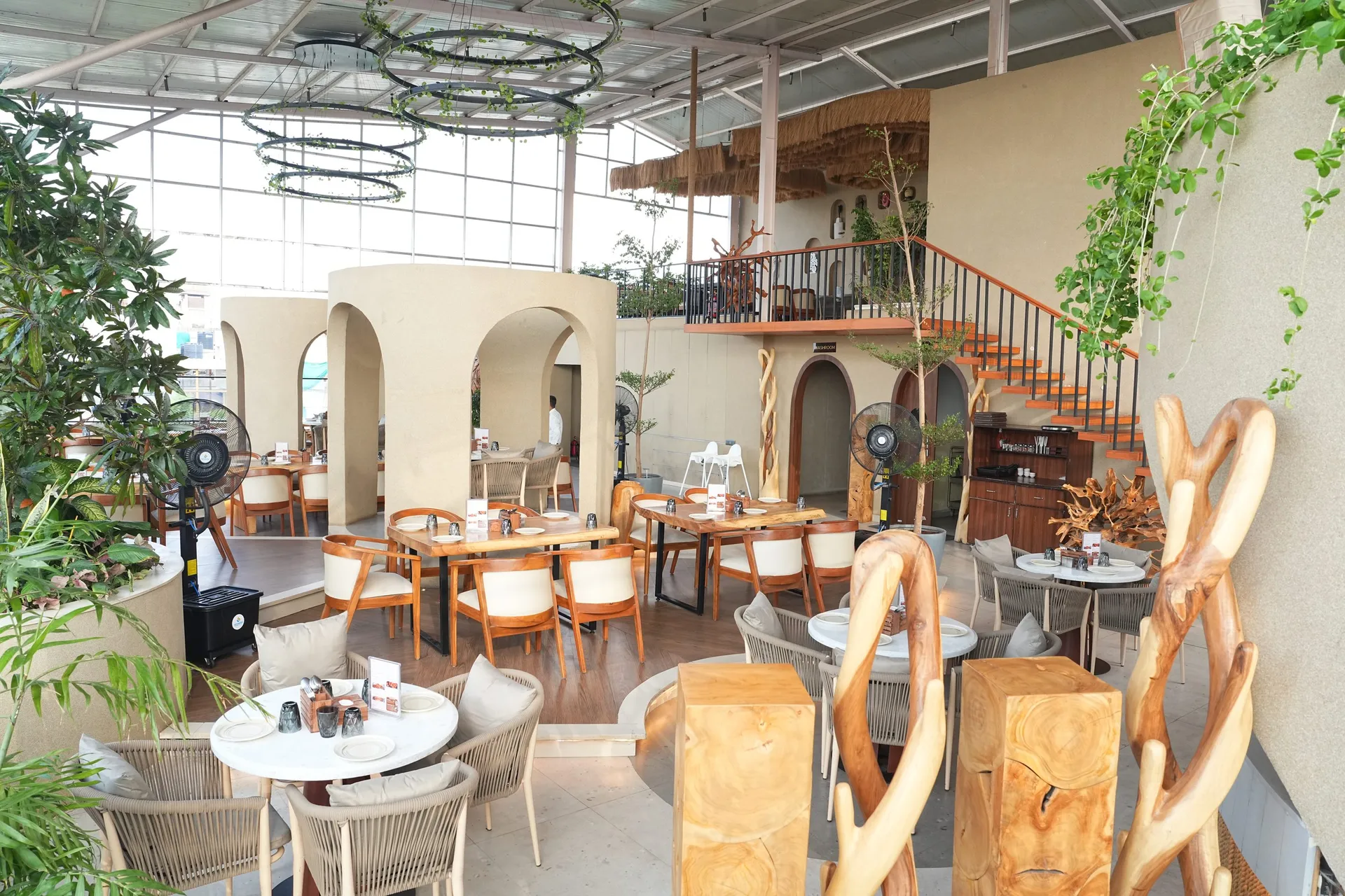 Dusk's rooftop dining room in daylight, with cream arches, wooden tables, hanging plants and a staircase to the upper deck
