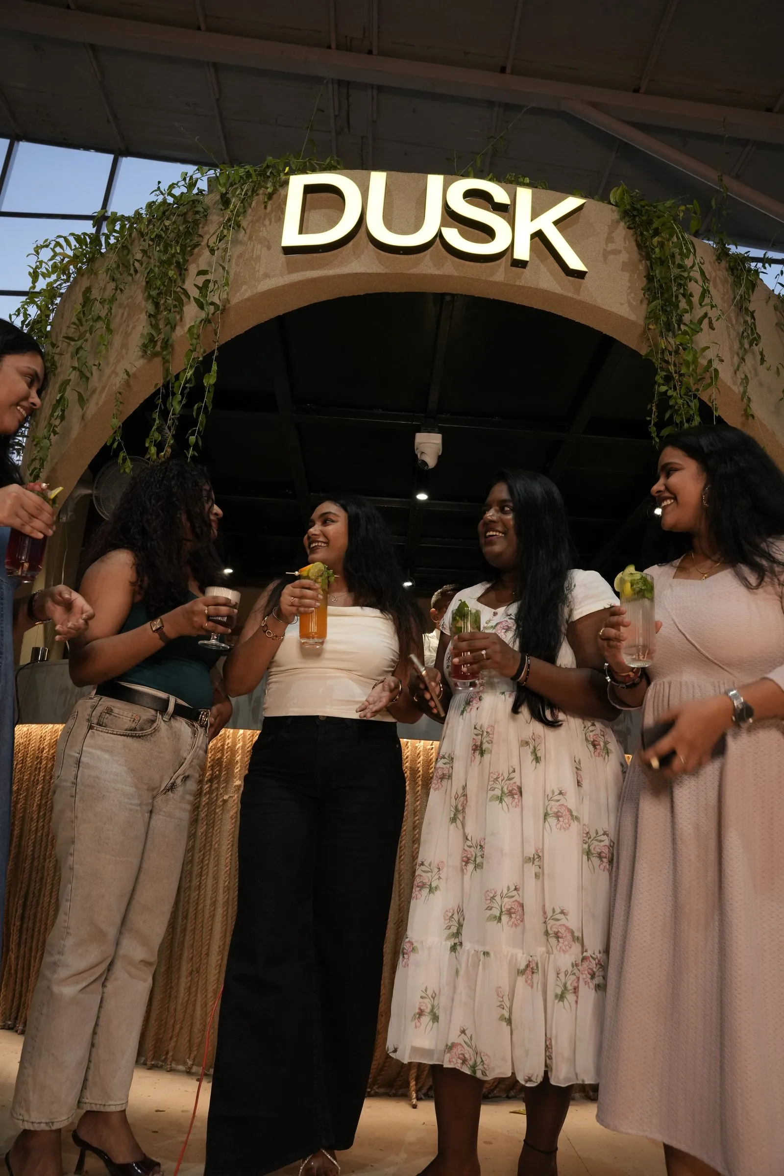 Friends laughing with mocktails beneath the glowing DUSK arch