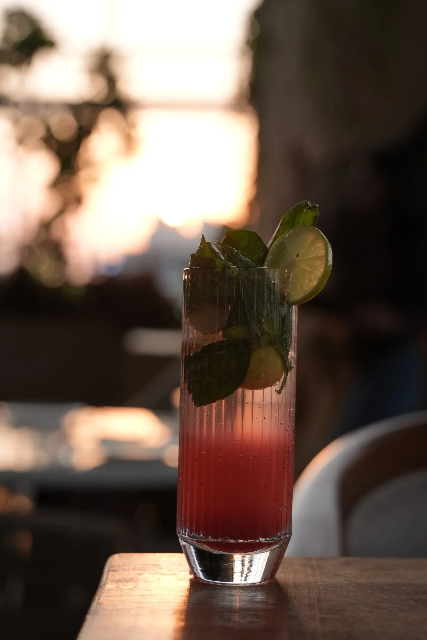 A tall watermelon-red mocktail with lime and mint against the sunset